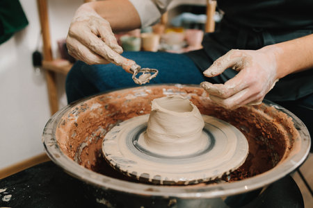 Potter sculpts a ceramic mug from clay in the pottery studio. Molding earthenware with potters toolsの写真素材