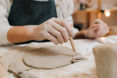Young potter cuts a circle of clay with pottery tool in the workshop. Preparing for clay modeling, closeupの写真素材