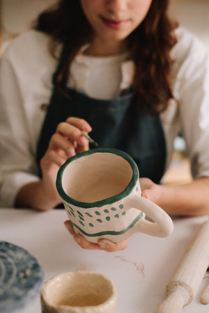 Potter draws an abstract design into earthenware cup. Experienced artist painting designs on ceramic...
