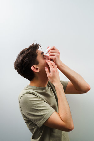 Man is using eye drops for allergy treatment. Man drips eye with eyes drops due to irritation problem. Applying eye drops for eye vision treatment at homeの写真素材