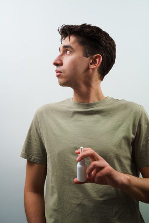 Nasal spray white bottle closeup in man's hands. Sinusitis treatment with pharmacy drops at homeの写真素材