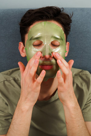 Man is applying facial mask for rejuvenate complexion, skincare concept. Relaxed man with hydrating...