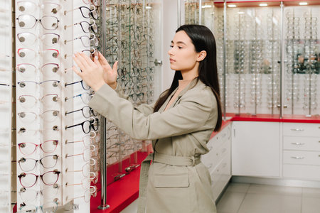 Woman chooses eyeglasses with clear lenses in the optician store. Large selection of eyeglasses with...