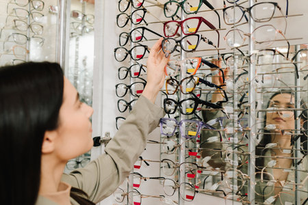 Female client chooses eyeglasses from the stand in the optical store. Large selection of eyeglasses with different frames. High quality eyeglasses with clear lensesの写真素材
