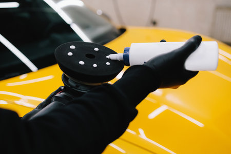 Professional car detailing. The master applies wax paste to the orbital machine for car body polishing at the serviceの写真素材