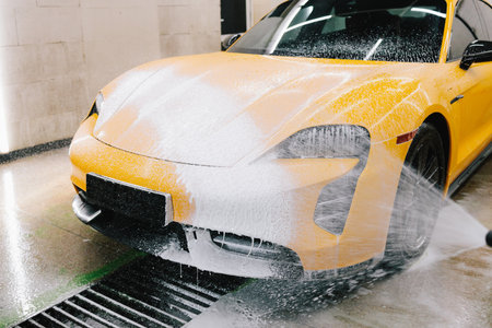 Application of soapy foam with a water gun for sports car cleaning at the service. Worker sprays soap solution with pressure from water jet for detailing car washの写真素材