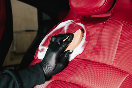 Man applies foam to red leather car seat for interior cleaning at the service. Car detailing process of cleaning leather auto seat with soap foam at the carwashの写真素材