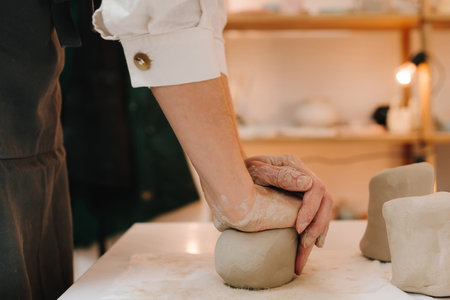 Craftswoman is preparing clay for making ceramic crockery. Female potter rolls piece of clay before...