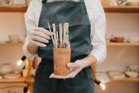 Clay crafting tools for ceramists. Potter in black apron holds a bunch of instruments for sculpting potteryの写真素材