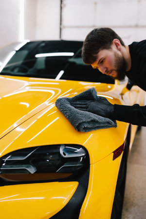 Mechanic detailing car uses a grey microfiber cloth to wipe the car. Cleaner wipes the body of a yellow car with a microfiber clothの写真素材
