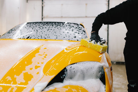Man washes the sports car using a soapy solution and sponge before detailing procedure. Meticulous car detailing concept at the car serviceの写真素材