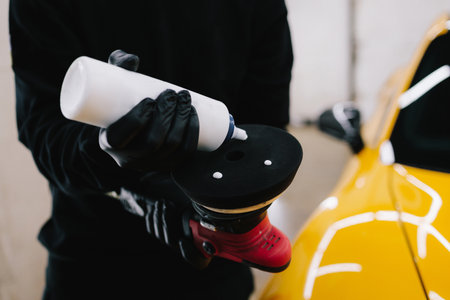 Professional car detailing. The master applies wax paste to the orbital machine for car body...