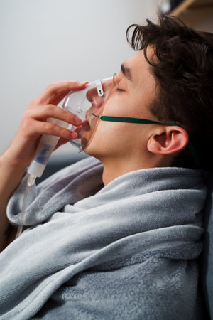 Patient inhaling through nebulizer for pneumonia treatment. Breathing with nebulizer for home virus treatmentsの写真素材