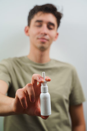 Nasal spray white bottle closeup in man's hands. Sinusitis treatment with pharmacy drops at homeの写真素材