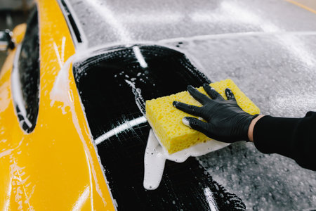 Sports car manual hand washing using foam and detergent with yellow sponge at the car washing service. Detailing sports car with foam at the auto serviceの写真素材