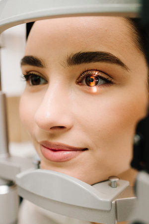 Ophthalmologist with slit lamp examines eyes and cornea of woman. Ophthalmologist illuminates eye of patient with light from slit lamp to diagnose the eyes and corneaの写真素材