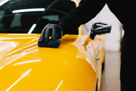 Detailing service worker applies ceramic protective liquid on the sports car. Smearing ceramic liquid to make protective nano layer for yellow sports carの写真素材