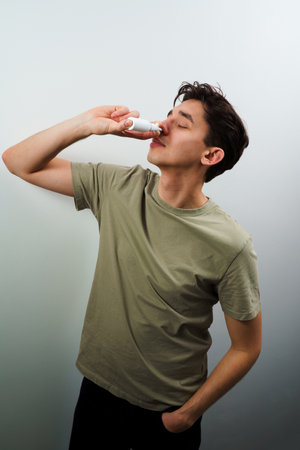 Sick guy injects nose drops for relief from runny nose at home. Man is using nasal spray medicament for treatmentの写真素材