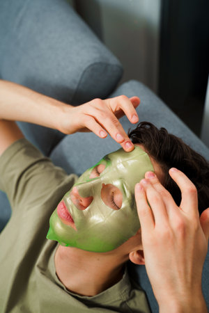 Young man using green face mask with hydrating effect. Male beauty procedures. Nourishing and pampering his skin with a hydrating and moisturizing facial maskの写真素材