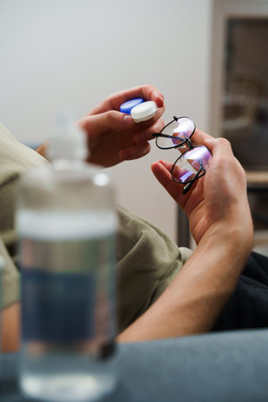 Man holds contact lenses plastic case and eyeglasses. Programmer is making choice between contact lenses and glasses for vision careの写真素材