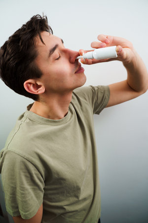 Sick guy injects nose drops for relief from runny nose at home. Man is using nasal spray medicament for treatmentの写真素材
