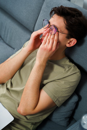 Tired man massages eyes after working on laptop. Suffering from eyesight problem after working with computerの写真素材