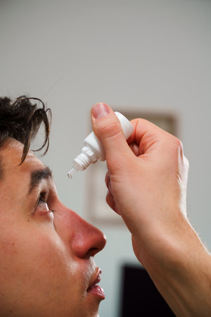 Man drips eye with eyes drops due to irritation problem. Applying eye drops for eye vision treatment at homeの写真素材