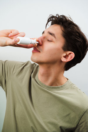 Sick guy injects nose drops for relief from runny nose at home. Man is using nasal spray medicament for treatmentの写真素材