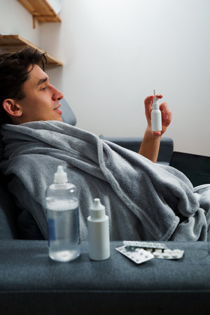 Man is taking medical pills and sprays by doctor's prescription at home. Sick patient takes nose drops for sinusitis treatmentの写真素材