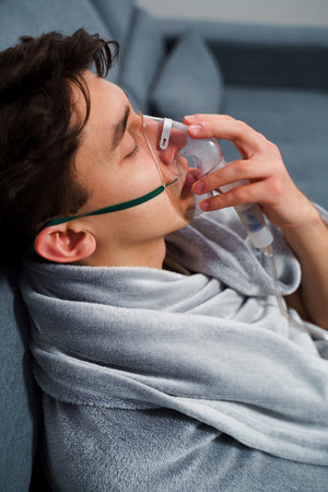 Patient inhaling through nebulizer for pneumonia treatment. Breathing with nebulizer for home virus treatmentsの写真素材