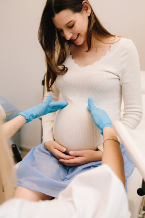 Palpation of womb belly, feeling baby fetus embryo bumps in gynecology clinic. Gynecologist is examining pregnant woman's belly during checkup in the clinicの写真素材