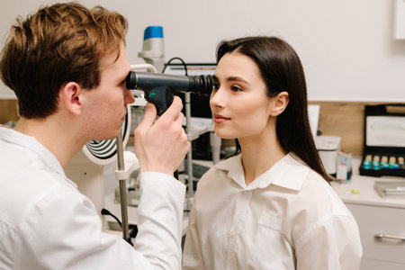 Ophthalmology consultation with an optometrist in a medical clinic. Ophthalmoscopy. Ophthalmologist examines the eyes of woman with ophthalmoscopeの写真素材