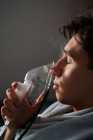 Using compressor nebulizer for disease treatment at home. Man inhaling through oxygen mask for cough treatmentの写真素材