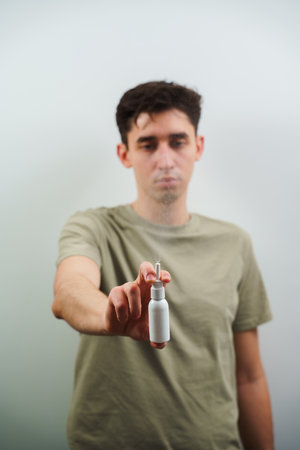 Sinusitis treatment with pharmacy drops on white background. Nasal spray white bottle closeup in man's handsの写真素材