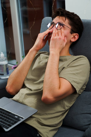 Tired IT specialist with headache in front of laptop. Eye tiredness from working remotely at homeの写真素材