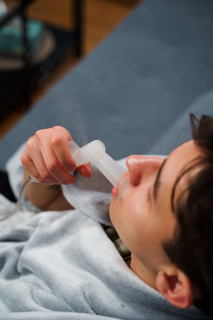 Sick man uses mouth inhaler nebulizer for flu treatment at home. Having mouth inhalation with the...
