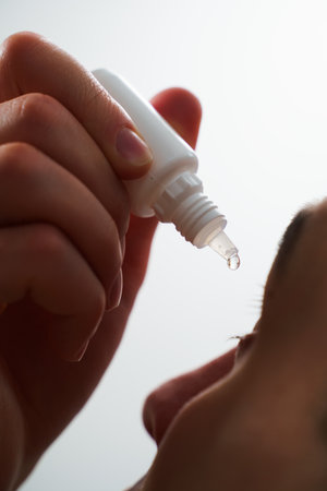 Man is applying eye drops at home. Young man is using eye drops for irritation problemの写真素材