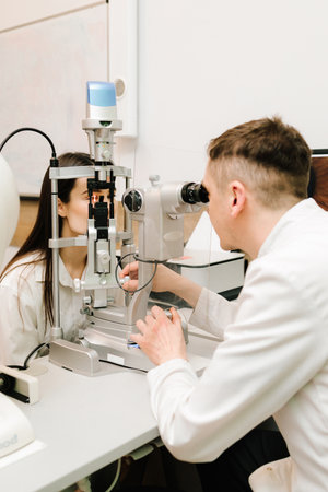 Ophthalmologist with slit lamp examines eyes and cornea of woman. Ophthalmologist illuminates eye of...