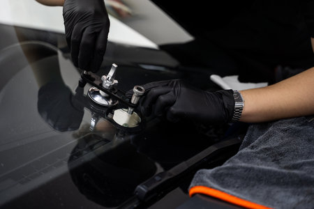 Technician uses a bridge tool to repair a car windshield crack with high-pressure resin injection. Windshield crack repair underway with a professional bridge tool and resinの写真素材