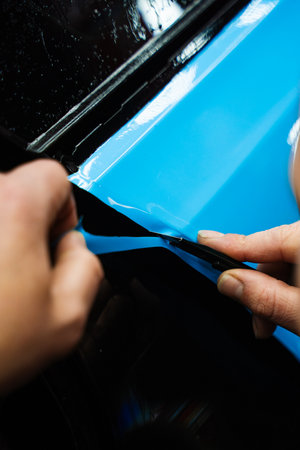 Precision cutting of PPF wrap on car body. Precision PPF wrapping and detailing on car panel using sharp blade to trim wrap with accuracy. Car detailing involves precise vinyl cutting techniquesの写真素材