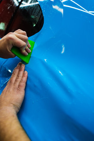 Blue PPF applied with green squeegee during detailing car to preserve finish and block damage. Applying a high-gloss blue PPF using a green squeegee ensures a bubble-free, smooth surface of carの写真素材