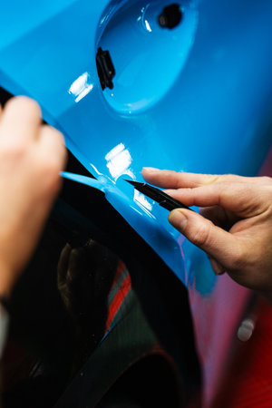 Precision cutting of PPF wrap on car body. Precision PPF wrapping and detailing on car panel using sharp blade to trim wrap with accuracy. Car detailing involves precise vinyl cutting techniques.の写真素材