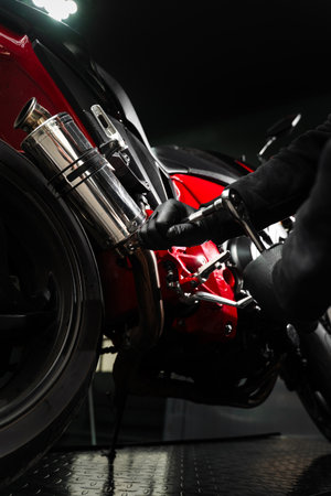 Mechanic tightening bolts on motorcycle chrome exhaust system for peak performance. Custom exhaust installation on red motorcycle enhances ride performance. Exhaust Motorcycle System Maintenanceの写真素材