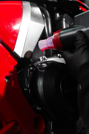 Motorcycle Oil Refill. Replacing engine oil in a sports motorcycle to ensure top performance and engine longevity. Precision oil fill operation on a red sportbike to ensure proper engine lubricationの写真素材