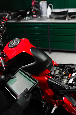 Motorcycle system diagnostic, scanning for faults across engine, electrical, and sensor modules to ensure reliability. Mechanic performing system diagnostics via tabletの写真素材