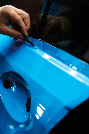 PPF Trimming with Precision Knife. Knife trimming in vinyl wrap detailing is crucial for perfection. Sharp blade is used to finalize the detailing process, cutting PPF wrap with exact precisionの写真素材