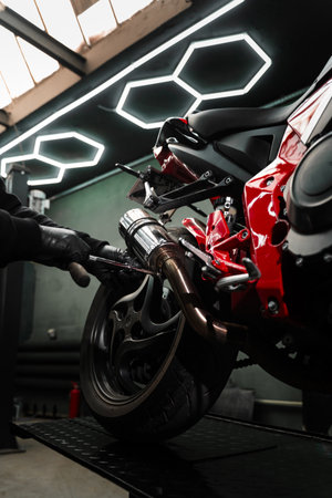Exhaust Motorcycle System Maintenance. Mechanic tightening bolts on motorcycle chrome exhaust system for peak performance. Custom exhaust installation on red motorcycle enhances ride performanceの写真素材