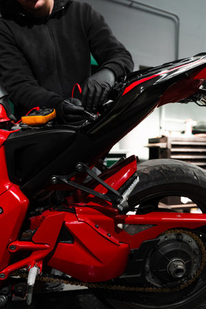 Digital multimeter reads motorcycle battery voltage during inspection. Mechanic testing battery with multimeter. Motorcycle battery is tested using digital multimeter to check voltage and healthの写真素材