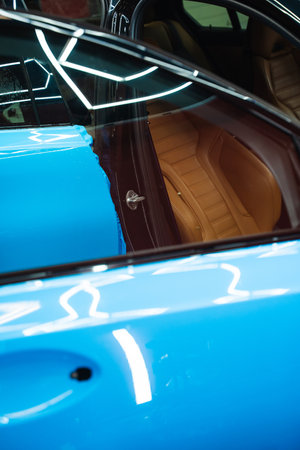 Bold blue vinyl wrap installing in detailing center. Detailers expertly apply wrap to fit contours and ensures smooth, flawless wrap alignment. Applying PPF wrap on car during full detailingの写真素材