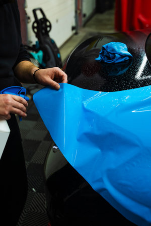 Detailing experts use hydration spray for controlled application of blue PPF film. Detailer uses spray-assisted method to apply vibrant blue vinyl wrap for perfect, bubble-free alignmentの写真素材